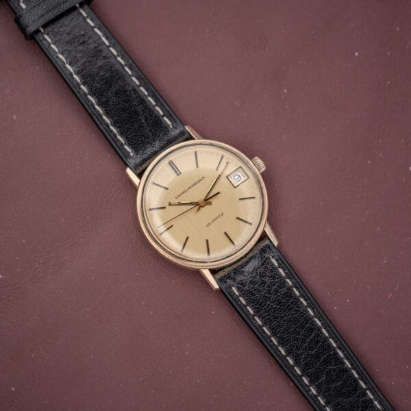 The Girard Perregaux Quartz Date 3696 with a champagne dial, black leather strap, and Cal. ETA 940 movement rests on a brown surface, featuring a quartz date display and date window.