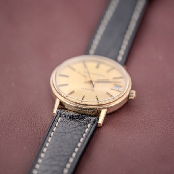 The Girard Perregaux Quartz Date 3696 Champagne Dial Cal. ETA 940, featuring a gold case and black leather strap, rests elegantly on a brown surface.