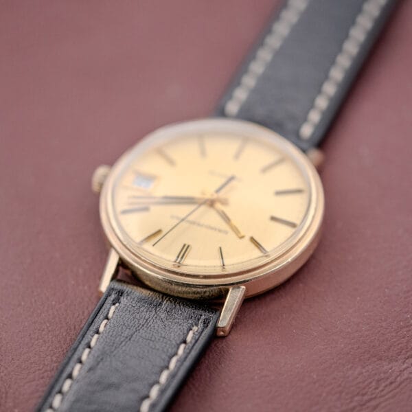 A Girard Perregaux Quartz Date 3696 with Champagne Dial (Cal. ETA 940) and a black leather strap rests elegantly on a maroon surface.