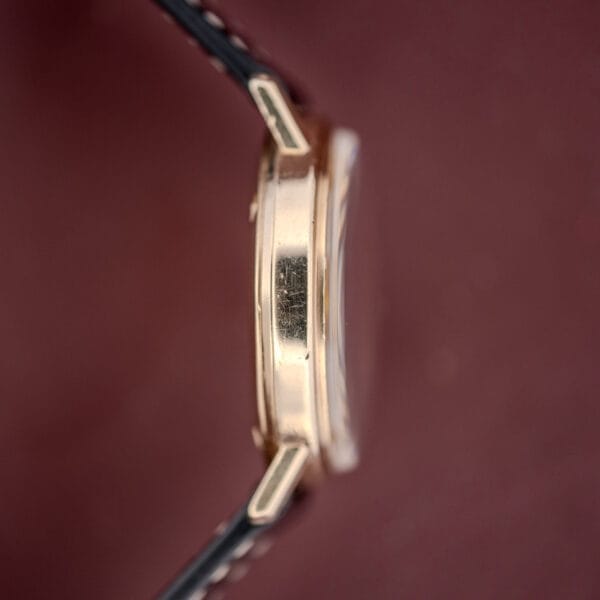 Side view of a Girard Perregaux Quartz Date 3696 with Champagne Dial and leather strap, Cal. ETA 940, displayed against a burgundy background.