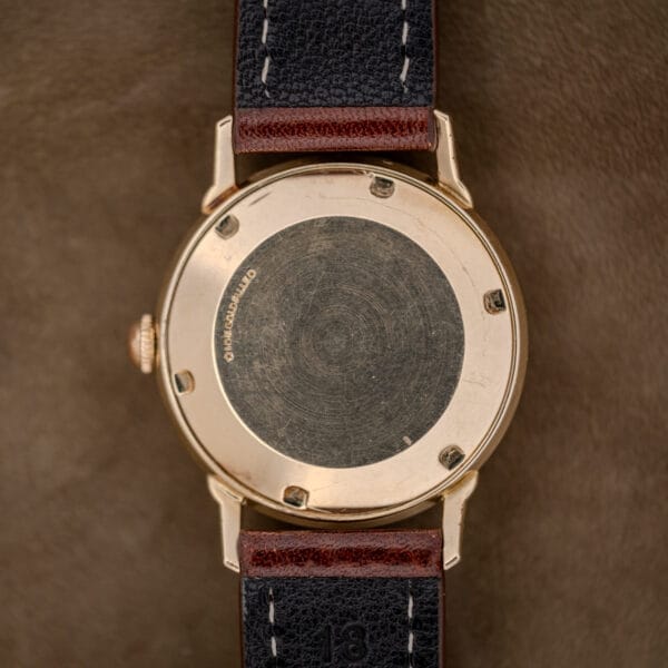 Close-up of the back of a Wittnauer Automatic Waffle Dial Ref. 2023 wristwatch with a 10k gold-filled case (Cal. 11ARB) and a brown and black leather strap, displayed on a brown surface.