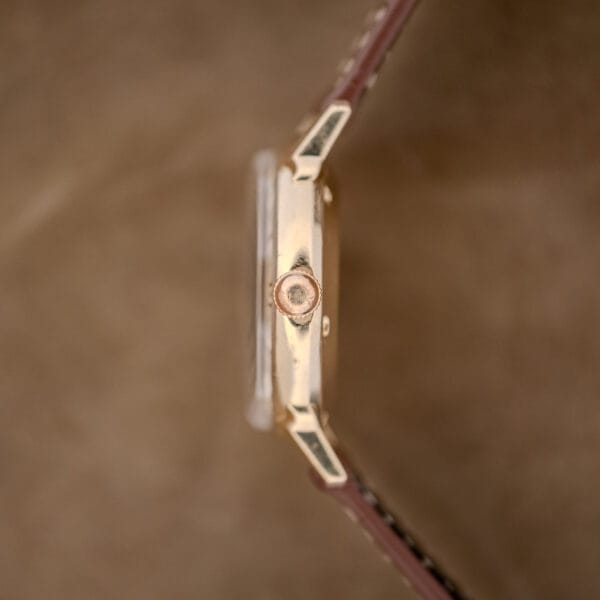 Side view of a Wittnauer Automatic Waffle Dial Ref. 2023 wristwatch with a 10k GF Case, Cal. 11ARB, and brown leather strap on a beige background.