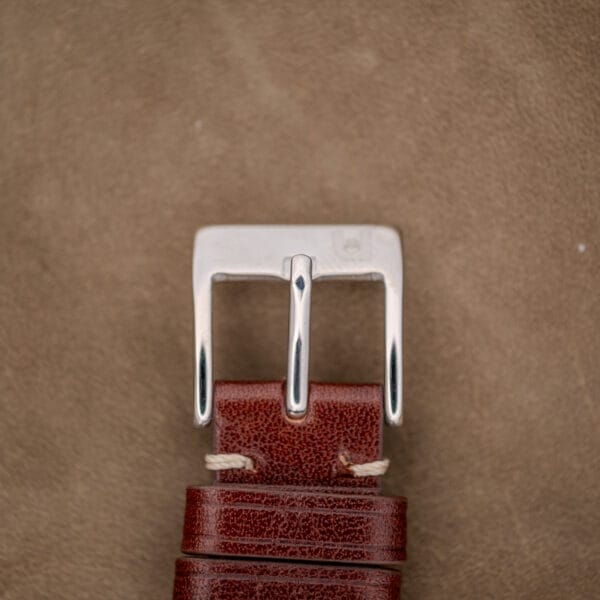 Close-up of a brown leather belt with a shiny silver buckle on textured brown, evoking the refined details of the Wittnauer Automatic Waffle Dial Ref. 2023 10k GF Case Cal. 11ARB.
