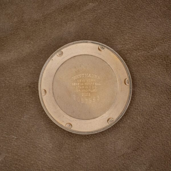 The Wittnauer Automatic Waffle Dial Ref. 2023 with a 10k GF case and Cal. 11ARB sits as a circular object on a brown surface.