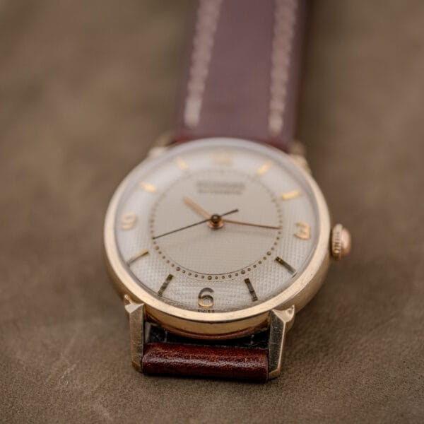A Wittnauer Automatic Waffle Dial Ref. 2023 wristwatch with a 10k GF case, Cal. 11ARB movement, brown leather strap, and gold details rests on a suede surface.