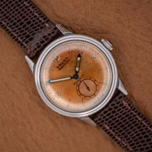 A Gruen Precision Auto-Wind Copper Dial in Stainless Steel Cal. 400 wristwatch with a brown leather strap rests on a tan textured surface.