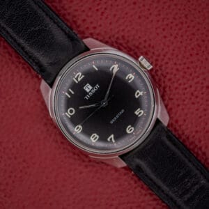 A Tissot Seastar Ref. 42568 with a matte black dial and stainless steel case (Cal. 781-1) is elegantly displayed on a red textured surface.