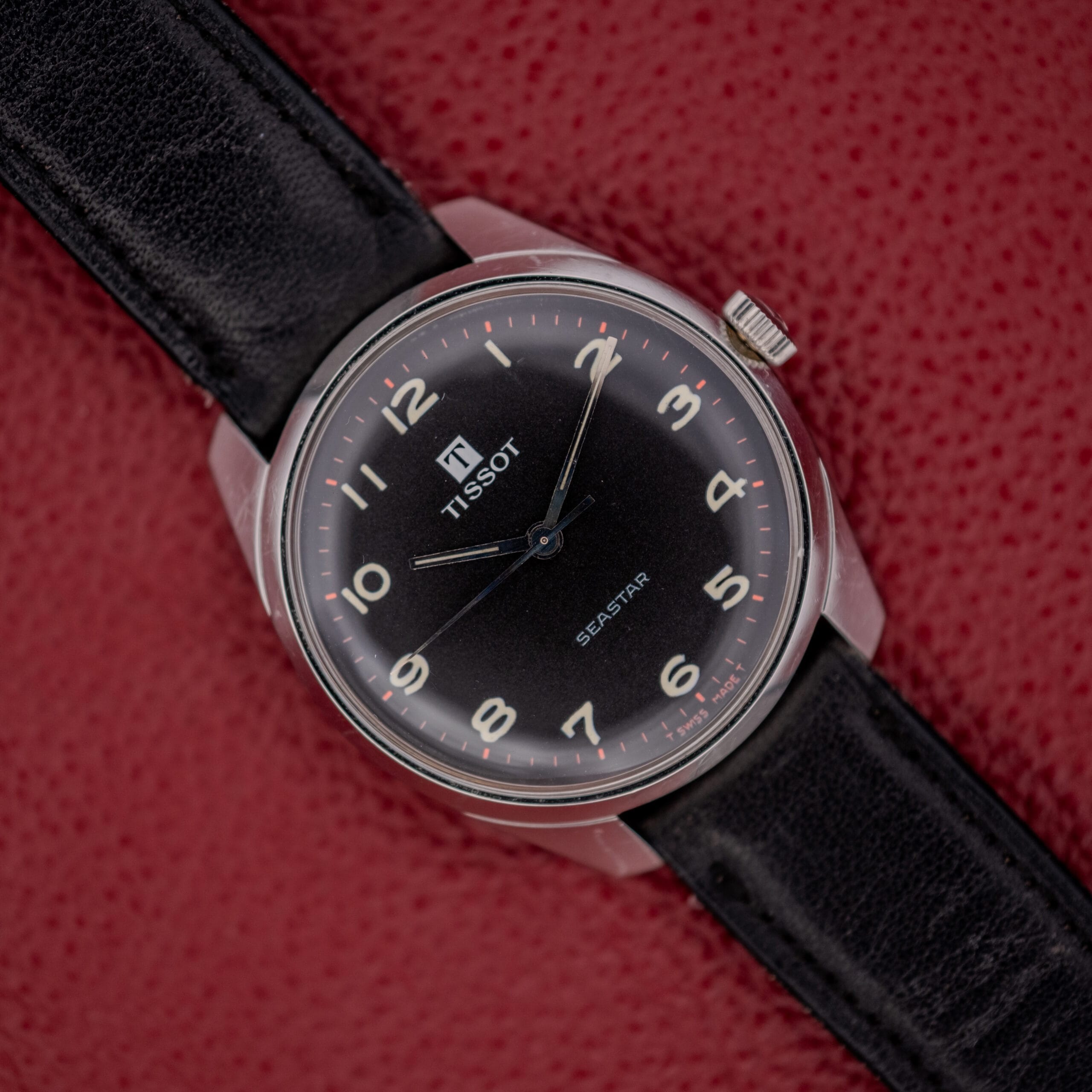 A Tissot Seastar Ref. 42568 with a matte black dial and stainless steel case (Cal. 781-1) is elegantly displayed on a red textured surface. A Tissot Seastar Ref. 42568 with a matte black dial and stainless steel case (Cal. 781-1) is elegantly displayed on a red textured surface.