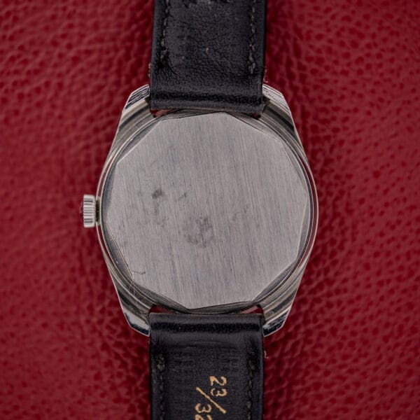 A Tissot Seastar Ref. 42568 with a matte black dial and stainless steel case on a black leather strap rests on a textured red surface.