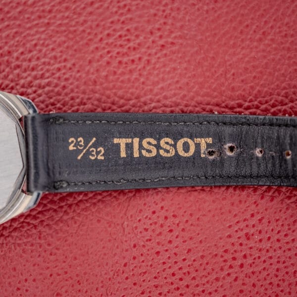 Close-up of the Tissot Seastar Ref. 42568, featuring a matte black dial and stainless steel case, with leather strap gold lettering set against a red textured background to highlight its elegance.