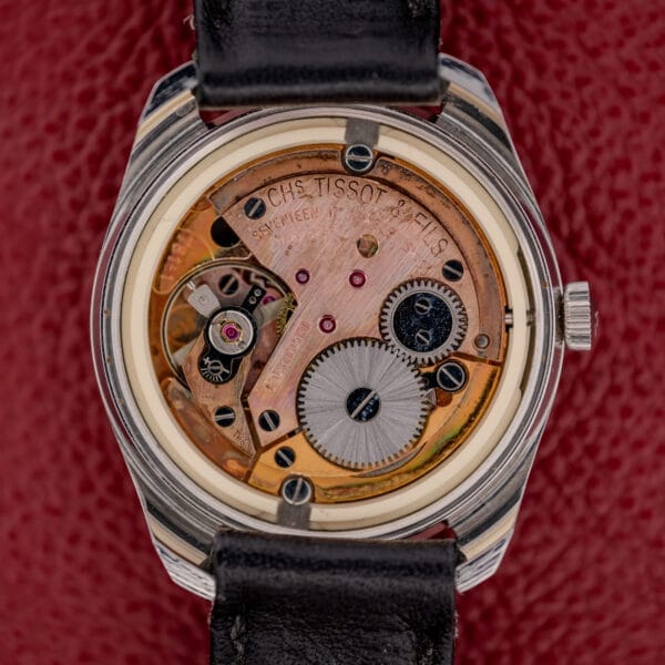 Close-up of a Tissot Seastar Ref. 42568 featuring a matte black dial and exposed Cal. 781-1 mechanical movement with visible gears, set against a red textured background.