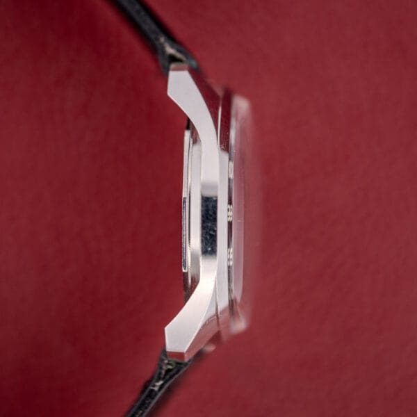 Side view of a Tissot Seastar Ref. 42568 wristwatch with a matte black dial and stainless steel case, Cal. 781-1, shown against a red textured background.