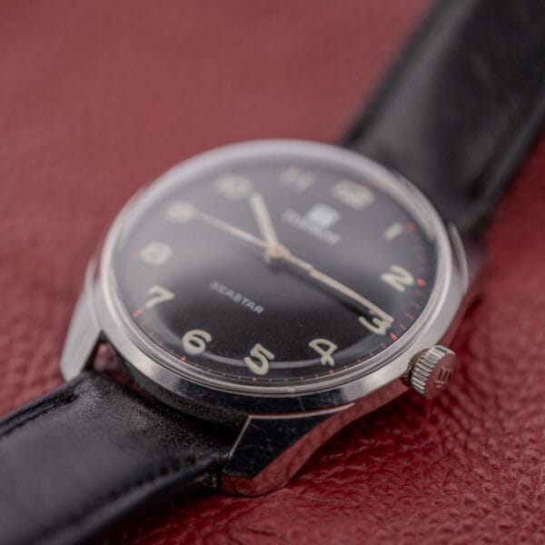 A close-up of the Tissot Seastar Ref. 42568, showcasing its matte black dial and stainless steel case (Cal. 781-1), displayed on a red textured surface.