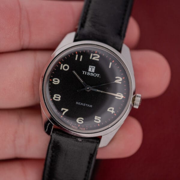 A hand holding a Tissot Seastar Ref. 42568 with a matte black dial, stainless steel case, and Cal. 781-1 movement.