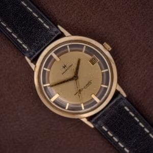 Hamilton Thin-O-Matic Brown & Gold Dial Automatic Cal. 624 wristwatch with black leather strap, displayed on a brown background.