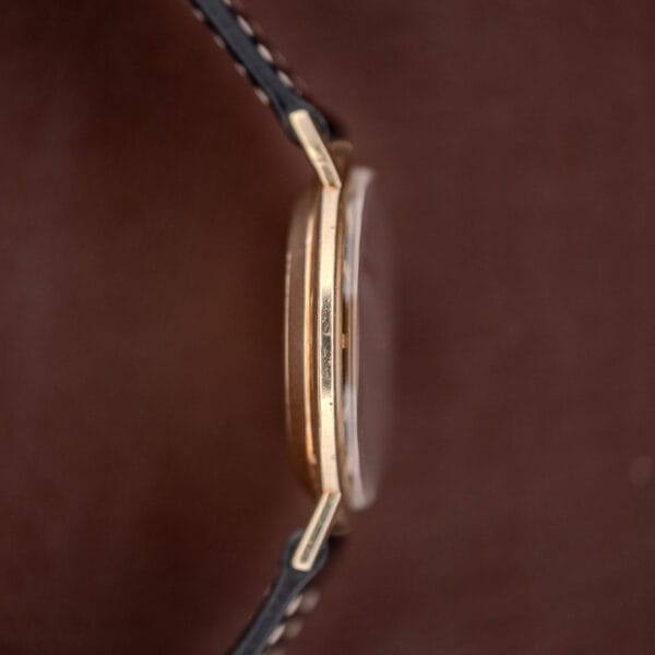 Side view of the Hamilton Thin-O-Matic Brown & Gold Dial Automatic Cal. 624 watch with a black leather strap, set against a brown background.