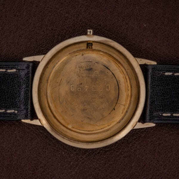 The back of a Hamilton Thin-O-Matic Brown & Gold Dial Automatic Cal. 624 wristwatch case, engraved with numbers, rests on a dark textured surface.