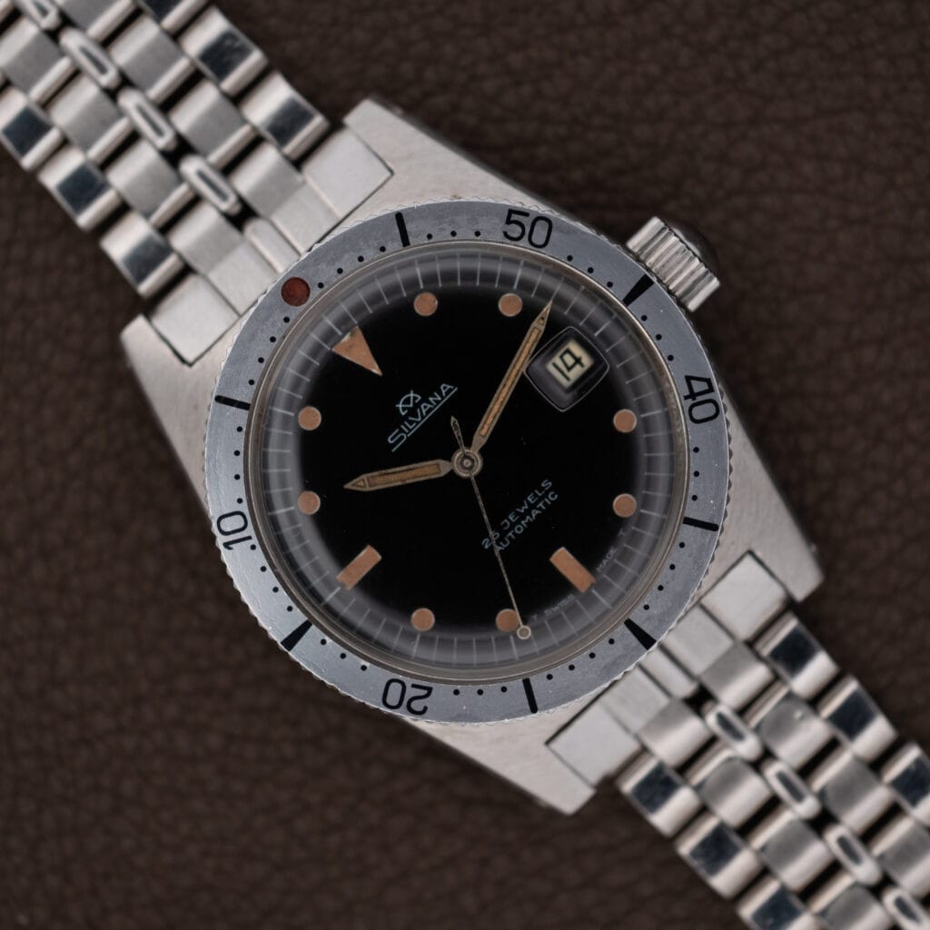 A Silvana 25 Jewels Automatic Skin Diver with Cal. 2472 movement, featuring a black dial and date display, is presented on a metal bracelet atop a brown surface.