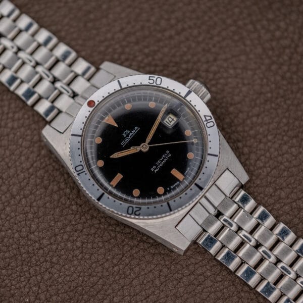 The Silvana 25 Jewels Automatic Skin Diver Cal. 2472 Black Dial wristwatch with a metal bracelet is displayed on a brown textured surface.