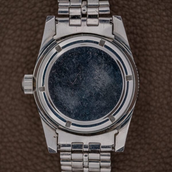 A close-up of the scratched back of a Silvana 25 Jewels Automatic Skin Diver Cal. 2472 Black Dial with metal band rests on a brown textured surface, highlighting its renowned Cal. 2472 movement.