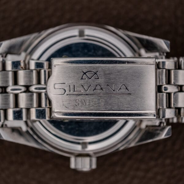 Close-up of a silver metal watch clasp engraved with Silvana Swiss, from the Silvana 25 Jewels Automatic Skin Diver Cal. 2472 Black Dial, set against a brown textured background.