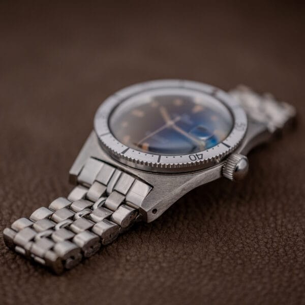 A close-up of a Silvana 25 Jewels Automatic Skin Diver Cal. 2472 wristwatch with a black dial and silver metal band, resting on a brown textured surface.