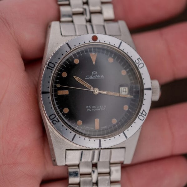 A hand holding a vintage Silvana 25 Jewels Automatic Skin Diver Cal. 2472 wristwatch with a black dial and silver metal band.