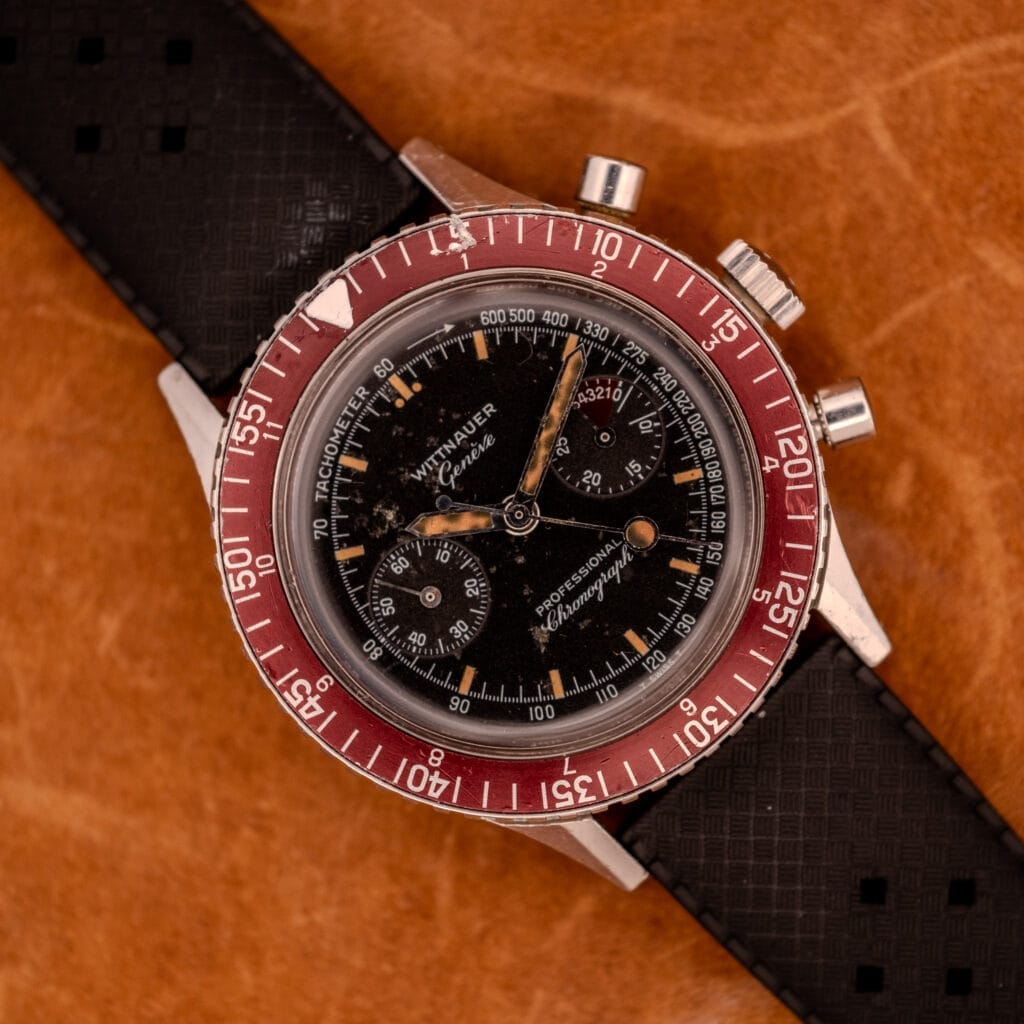 Wittnauer Professional Chronograph Ref. 7004 Landeron 248 with a red bezel, black dial, and black strap rests on a brown leather surface.