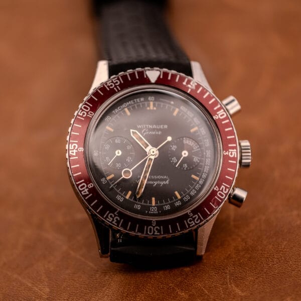 A vintage Wittnauer Professional Chronograph Ref. 7004 Landeron 248 featuring a vibrant red bezel and black strap, elegantly displayed on a brown surface.
