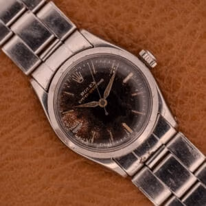 A Rolex Oyster Speedking Ref. 6420 with a stainless steel band and black dial rests on a brown surface.