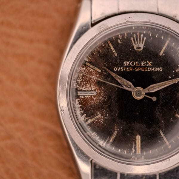 Close-up of a vintage Rolex Oyster Speedking Ref. 6420 with a worn stainless steel band and a damaged black dial.