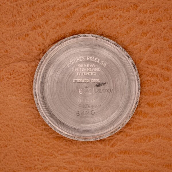 The Rolex Oyster Speedking Ref. 6420 Stainless Steel Black Dial features a round stainless steel case back engraved with its branding and reference number, shown resting on a brown textured surface.