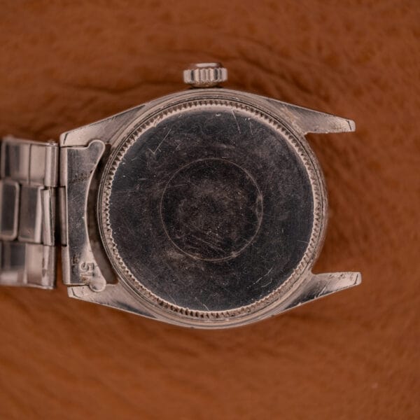 A close-up of the back of a scratched Rolex Oyster Speedking Ref. 6420 Stainless Steel Black Dial watch case, without its strap, on a brown surface.