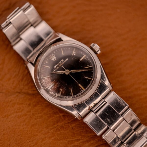 A Rolex Oyster Speedking Ref. 6420 Stainless Steel Black Dial wristwatch with a worn band is displayed on a brown leather surface.