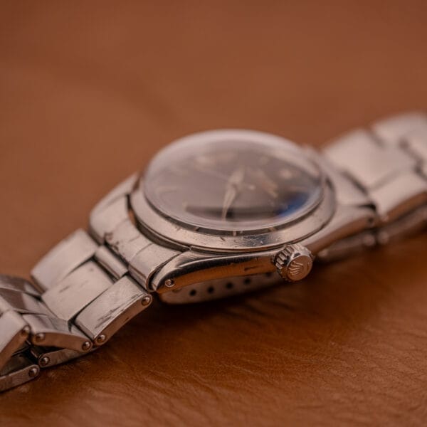 A close-up of a scratched Rolex Oyster Speedking Ref. 6420 Stainless Steel Black Dial with a metal band, shown resting on brown leather.