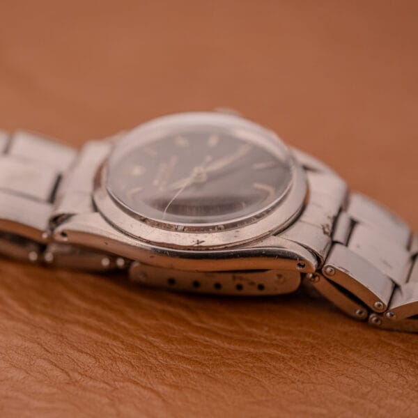 Close-up of a Rolex Oyster Speedking Ref. 6420 Stainless Steel Black Dial wristwatch with a metal band, resting on a brown leather surface.