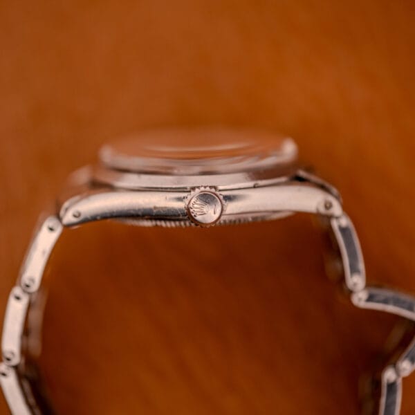 Close-up side view of a Rolex Oyster Speedking Ref. 6420 Stainless Steel Black Dial wristwatch with a crown logo, set against a brown background.