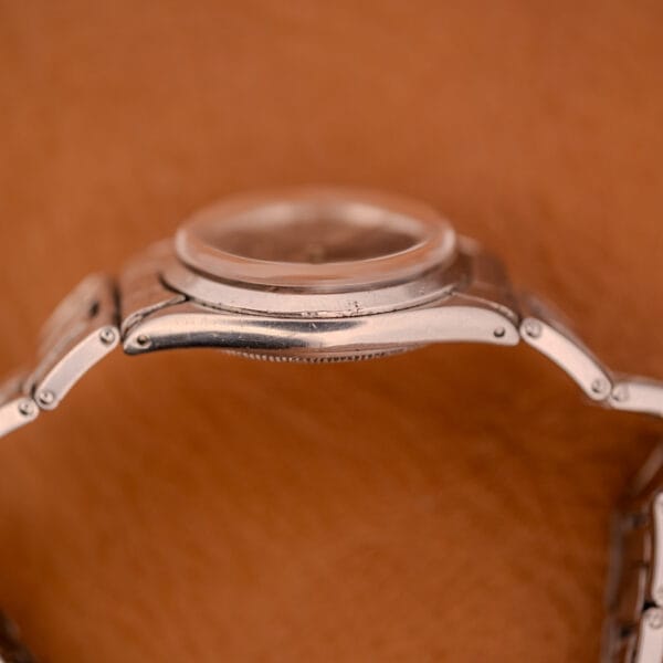 Side view of a Rolex Oyster Speedking Ref. 6420 Stainless Steel Black Dial wristwatch with a metal band, displayed against a tan background.