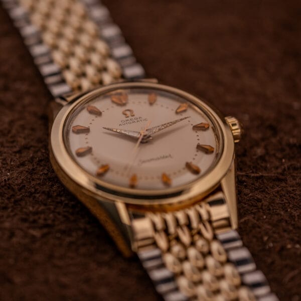 An Omega Seamaster "De Luxe" Ref. 2802 Automatic Cal. 471 wristwatch in gold and silver rests elegantly on a brown textured surface.