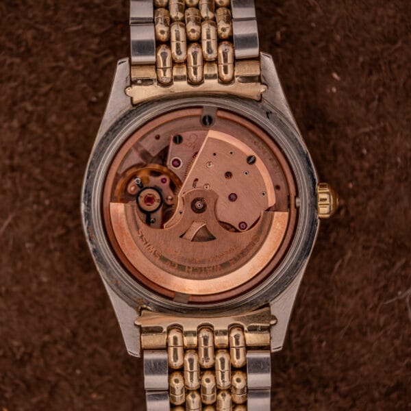 Close-up of an Omega Seamaster "De Luxe" Ref. 2802 showing its exposed Automatic Cal. 471 movement and two-tone metal band on a brown background.