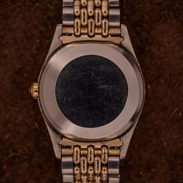 Close-up of the back of an Omega Seamaster "De Luxe" Ref. 2802 Automatic Cal. 471 wristwatch with a two-tone linked band, displayed on a brown background.