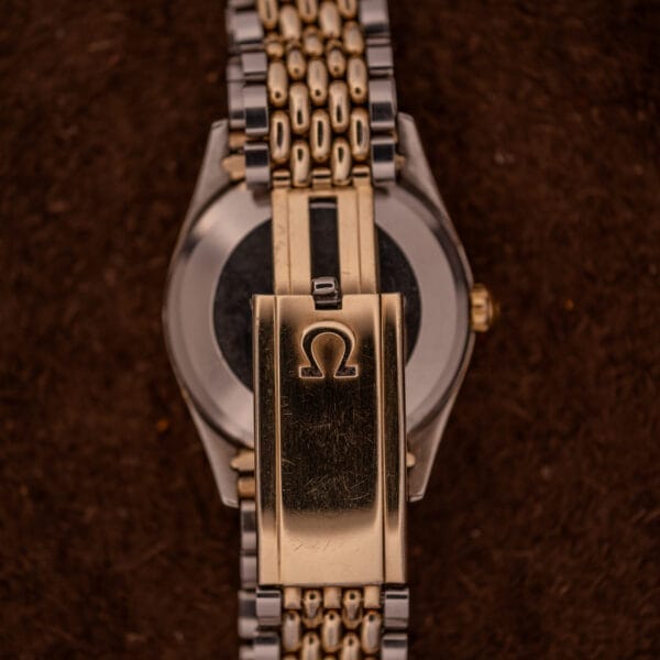 Close-up of the clasp on an Omega Seamaster "De Luxe" Ref. 2802 Automatic Cal. 471 bracelet, featuring the Omega logo, set against a dark brown background.