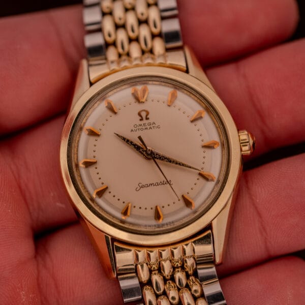 An Omega Seamaster "De Luxe" Ref. 2802 automatic watch with a cream dial and Automatic Cal. 471 movement is held in a person's hand.