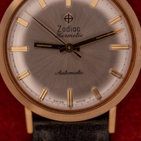 Close-up of a Zodiac Hermetic Sunburst Dial Automatic watch with a 10k gold-filled case, silver face, gold markers, and black leather strap.