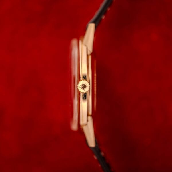 Side view of a Zodiac Hermetic Sunburst Dial wristwatch with a 10k gold filled case and black strap, set against a vibrant red background.