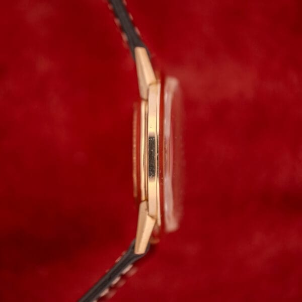 A Zodiac Hermetic Sunburst Dial 10k Gold Filled Case Automatic wristwatch is shown from the side against a red background, displaying its black strap.