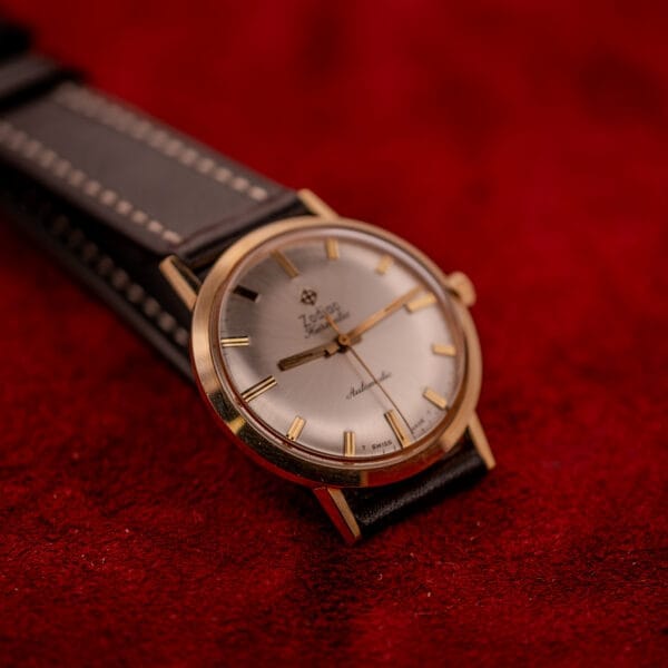 The Zodiac Hermetic Sunburst Dial 10k Gold Filled Case Automatic wristwatch with a black leather strap rests on a red textured surface, highlighting its striking gold vintage design.