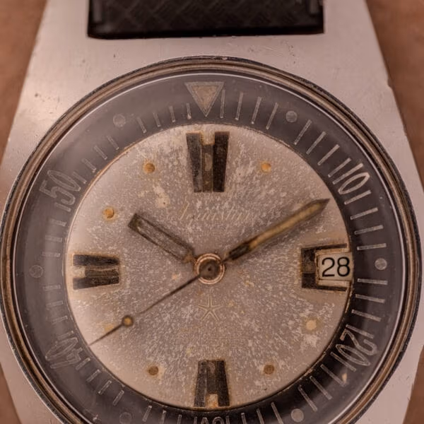 Close-up of Aquastar 1701 dial showing cursive Aquastar signature, oxidized baton markers, sword hands with darkened lume, date window at 3 reading 28.