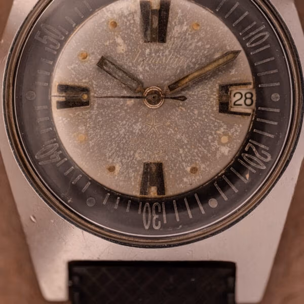 Macro of Aquastar 1701 dial with Aquastar star logo under the center pinion, depth-rating text faintly visible through the mottled silver-grey patina.