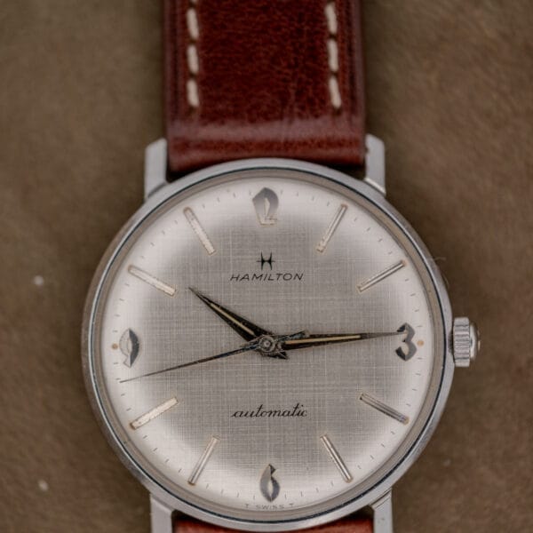 A Hamilton Automatic Silver Linen Dial Stainless Steel Cal. 689A wristwatch with a brown leather strap rests on a beige surface.